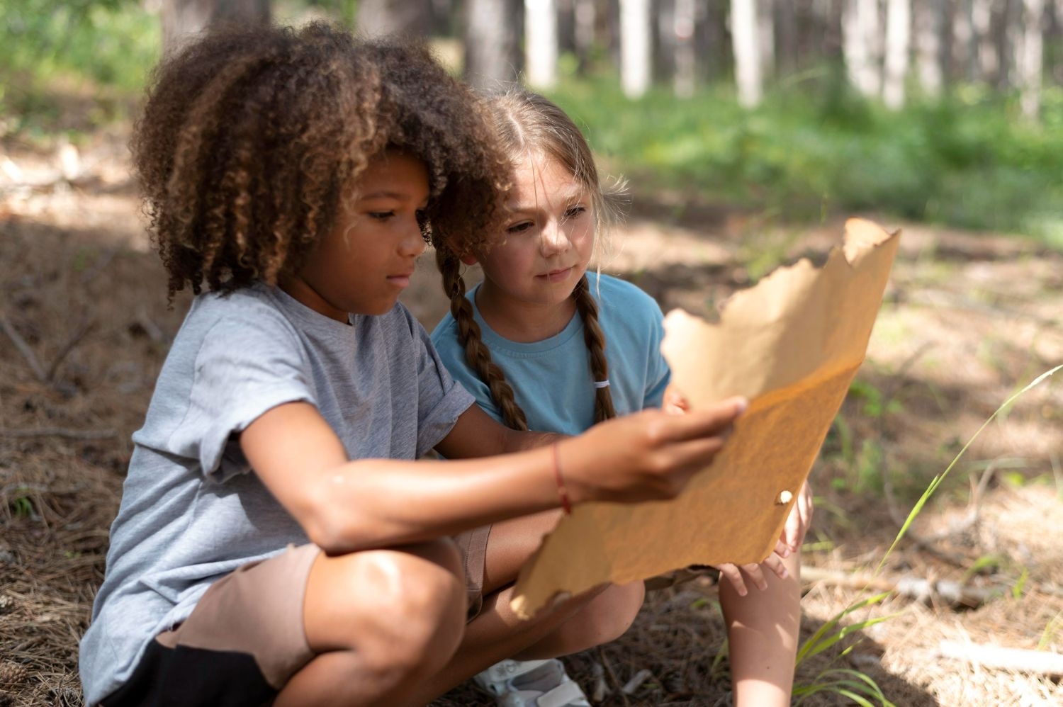 two school age campers sitting outside studying a hand drawn map at summer camp