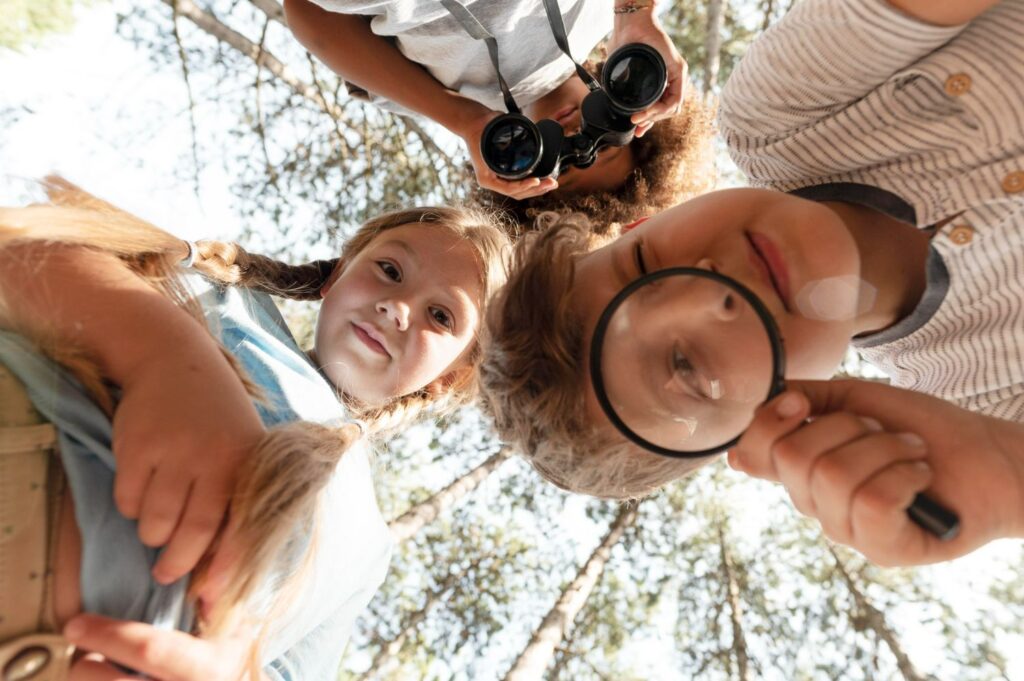 elementary age children studying nature at summer camp with magnifying glass and binoculars