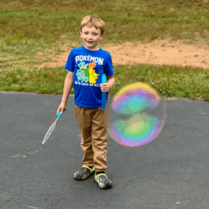 boy blowing huge bubble at ymca summer camp, outdoors in grass