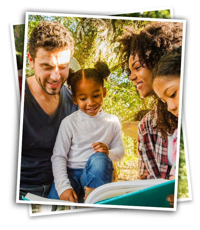 Mixed race family taking hike in woods on a camping trip and looking at their nature joural