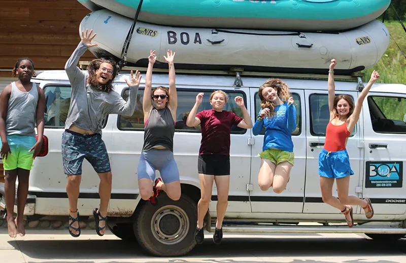 kids cheering at Camp Horizons in the Shenandoah Valley of Virginia as they set off on a rafting trip, van with rafts in background.