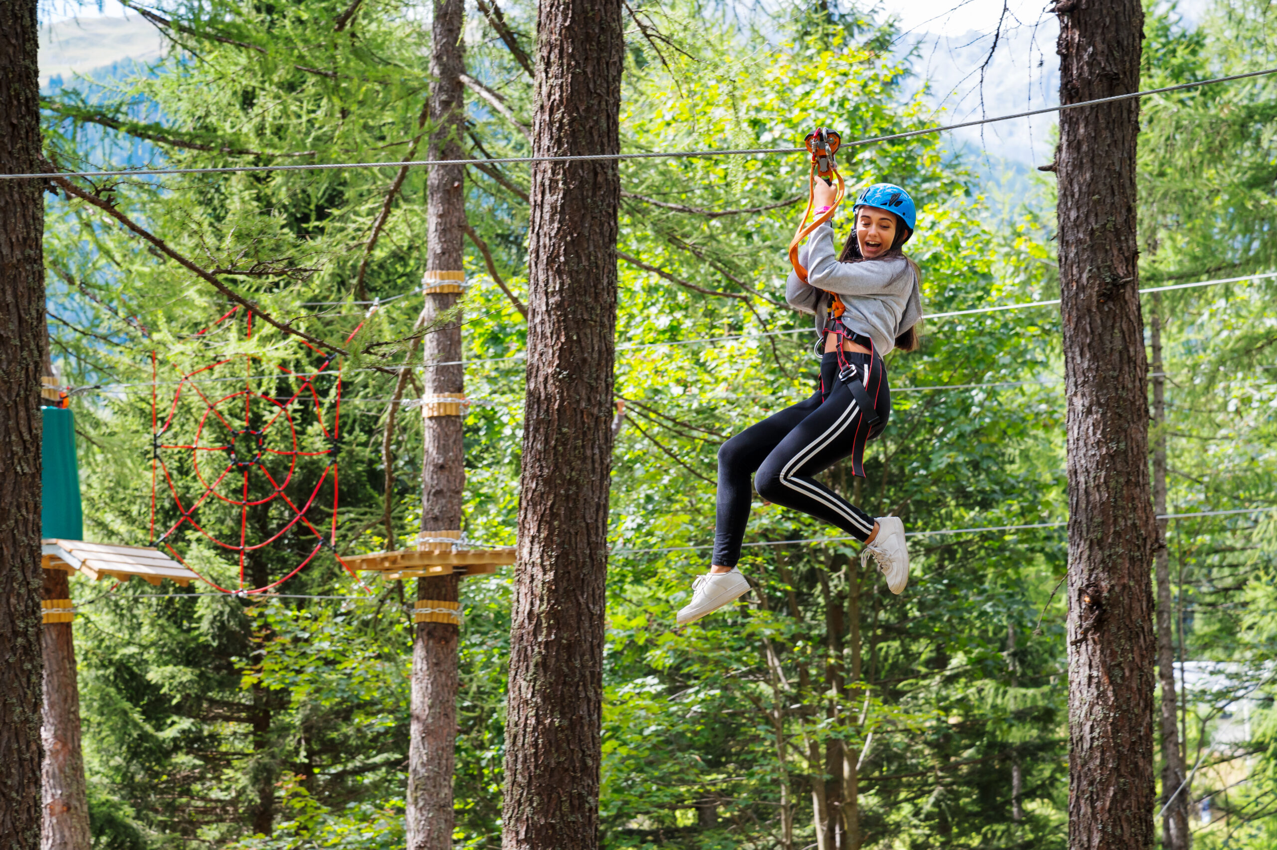 Happy teen on zipline among the trees at Virginia summer camp - adventure sports. Building confidence by trying new challenges. wearing safety gear.