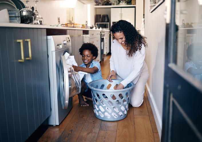 Adorable little African American boy with an afro smiling and having fun while doing housework with him mother at home. mixed race shot of a cute child folding laundry with his mom
