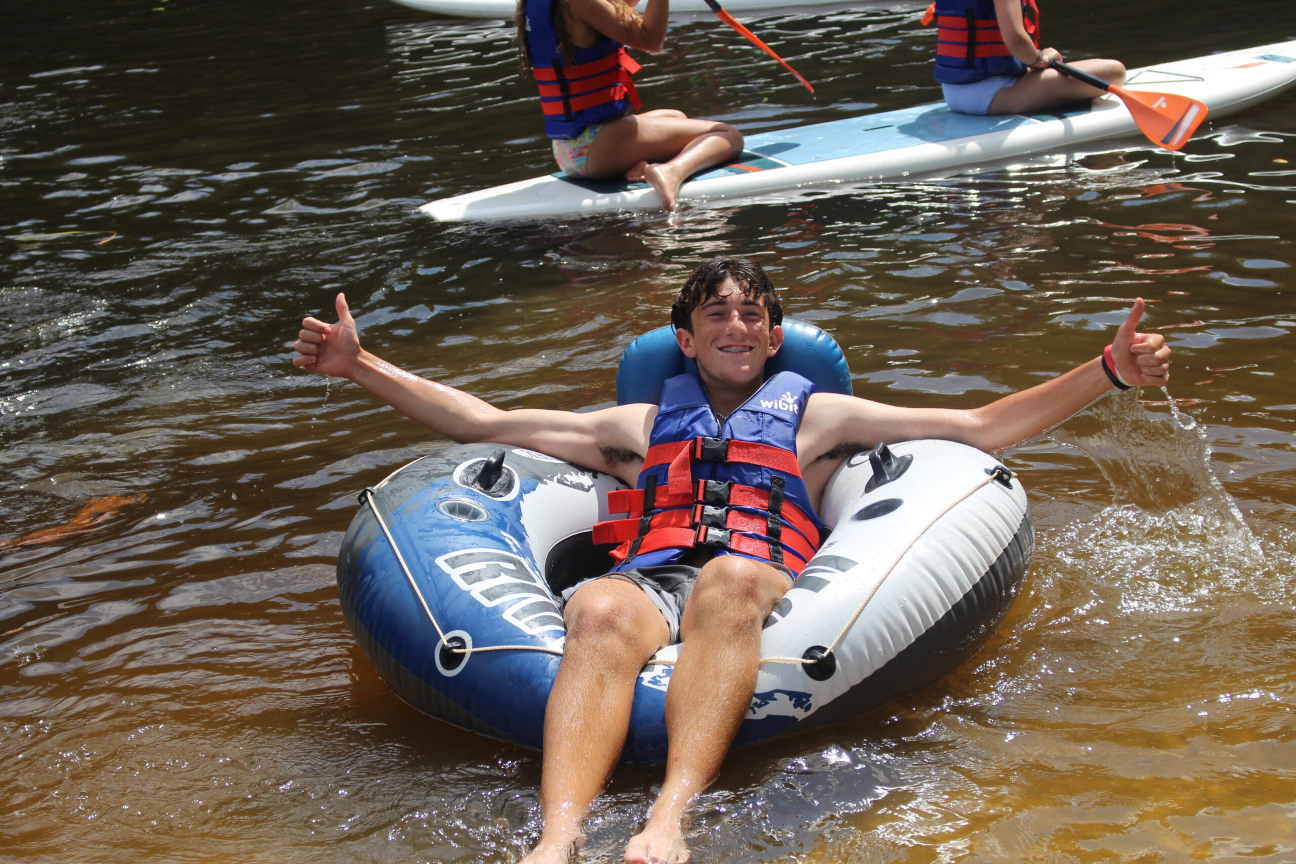 teen boy smiles in inner tube on lake at Twin Creeks Camp
